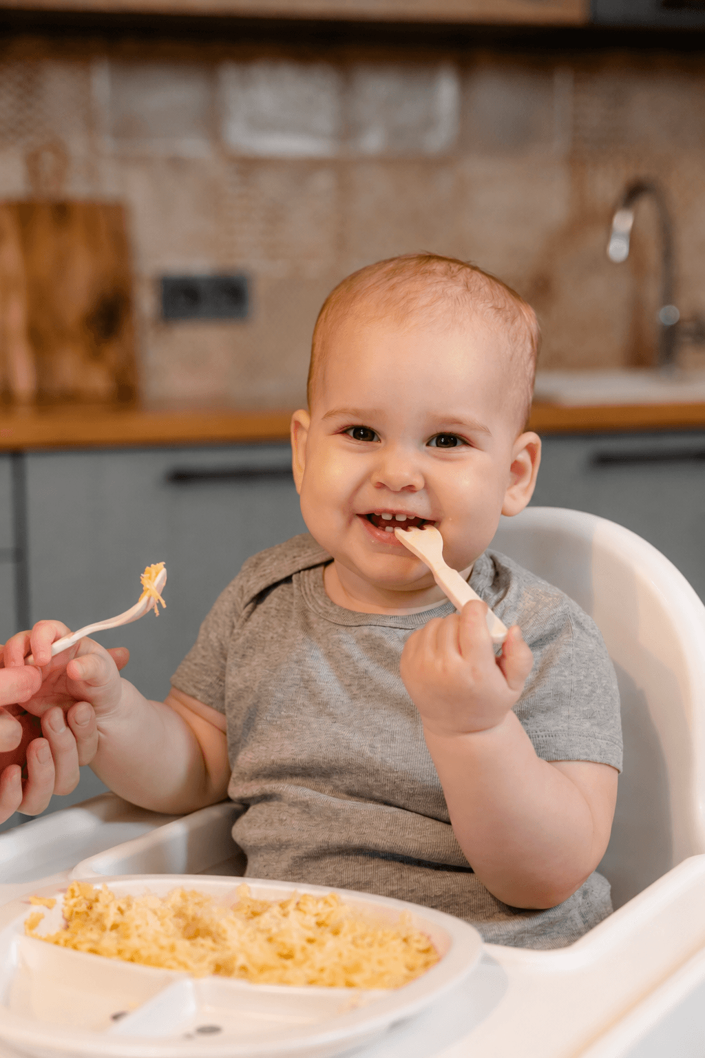 Mama sandalyesinde kaşıkla ek gıda yiyen bebek